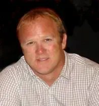 Portrait of a smiling person in a checkered shirt against a dark background.