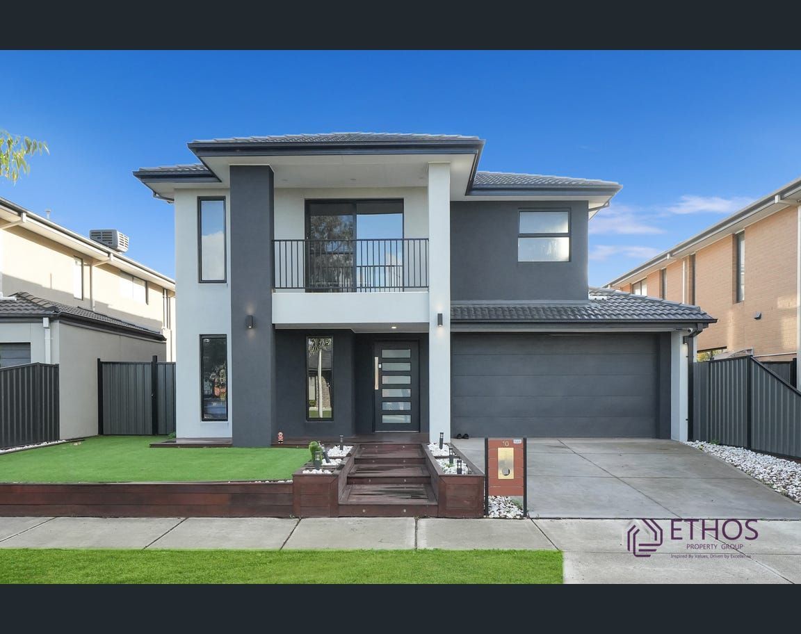 Two-story modern house with a gray facade, garage, and balcony; a green lawn and clear sky are in the foreground.
