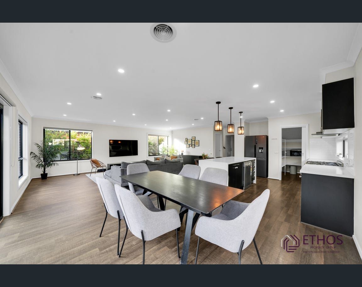 Open-concept living and dining area with a dark dining table and white chairs, featuring a large couch, TV, and kitchen.