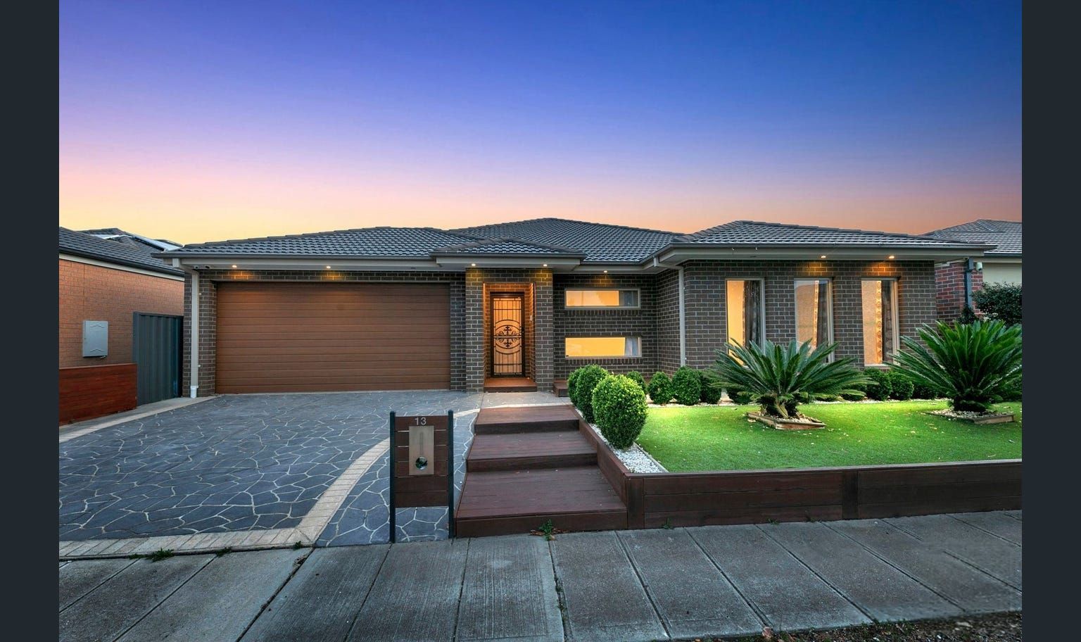 Modern home with a brick facade, wooden garage door, and manicured lawn. Evening sky above.