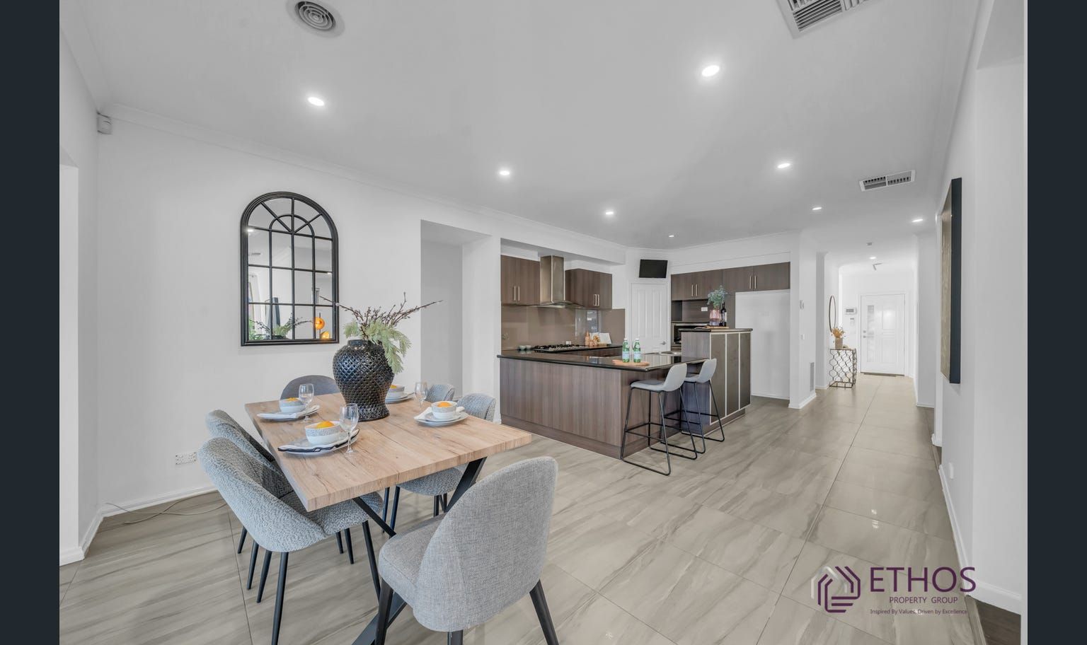 A modern dining area with a wooden table, gray chairs, and an open kitchen with dark cabinets and stainless steel appliances.