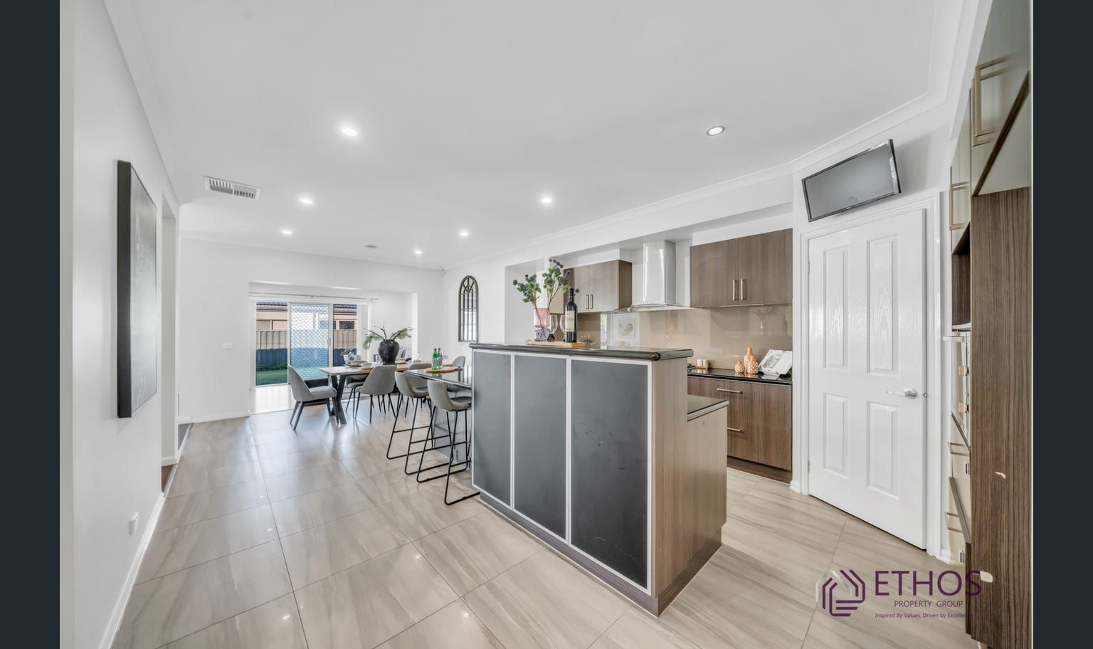 Open-plan kitchen and dining area with a dark island, wood cabinets, and access to an outdoor patio.