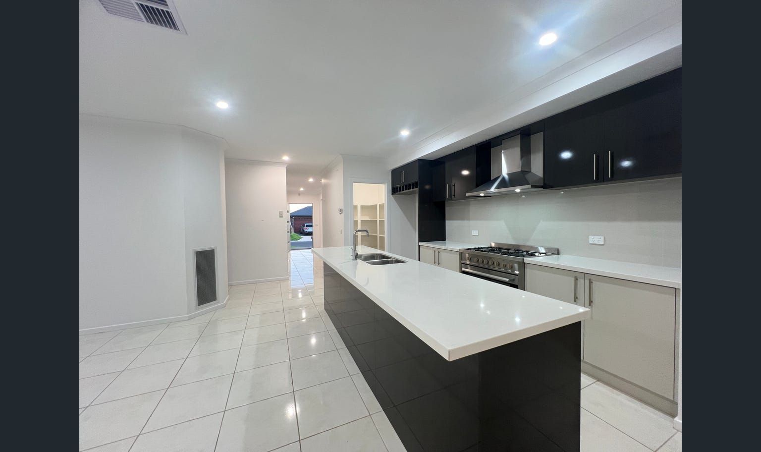 Modern kitchen with a white countertop island, dark cabinetry, and stainless steel appliances. The floors are white tile.