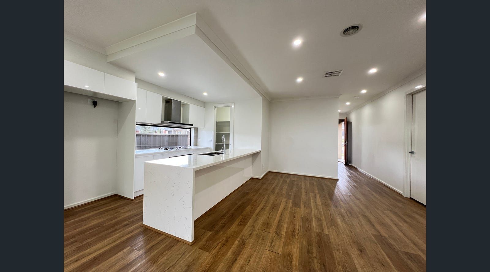 Modern kitchen and living area with white cabinetry, stainless steel appliances, wooden floors, and a long island.