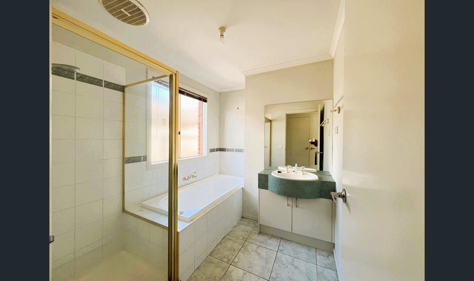 Bathroom with a built-in bathtub, shower, and vanity. The room has white tiles and a gold shower frame.
