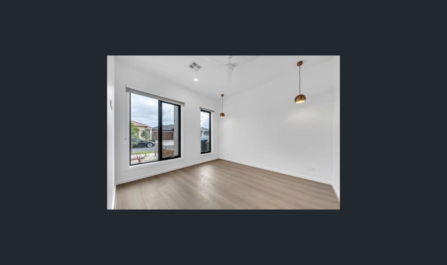 Empty room with two windows, wood floors, and a hanging light fixture.