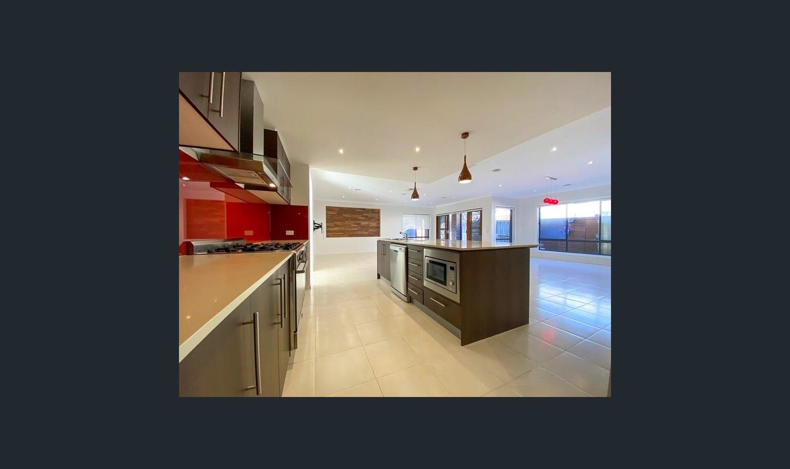Modern kitchen with a large island, stainless steel appliances, and red backsplash.