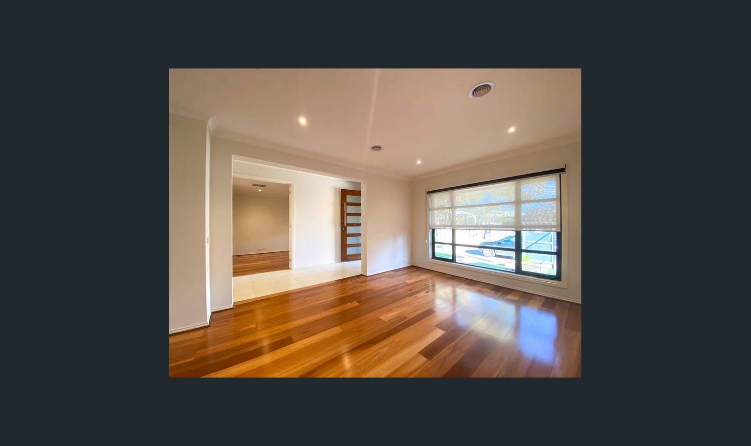 Empty room with polished wooden floors and large window, doorway leading to another room.