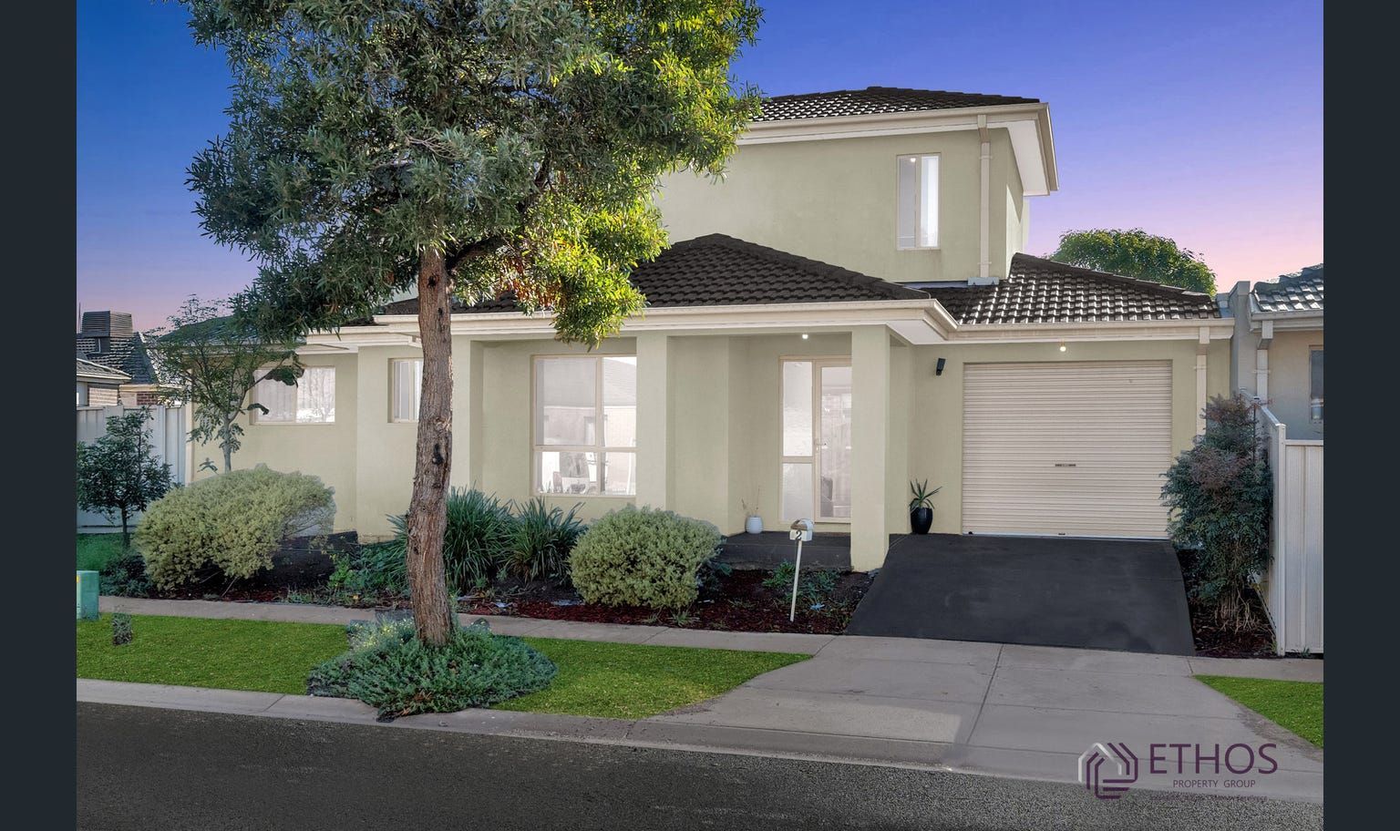 Two-story home with a green facade, small front yard, and a driveway leading to a garage.