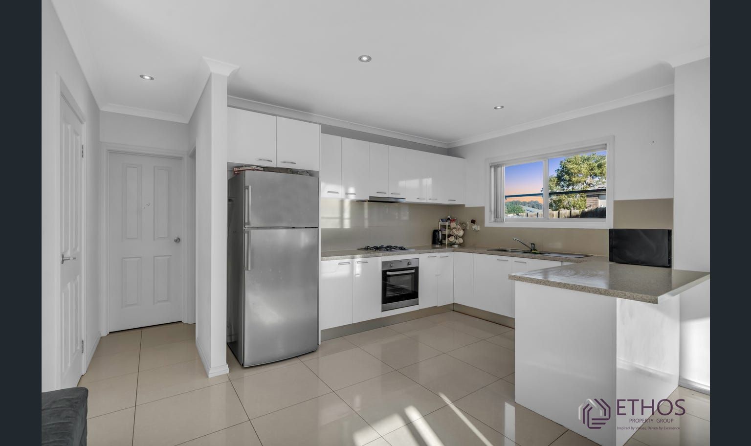 Bright, modern kitchen with white cabinets, stainless steel appliances, and a window overlooking the outside.
