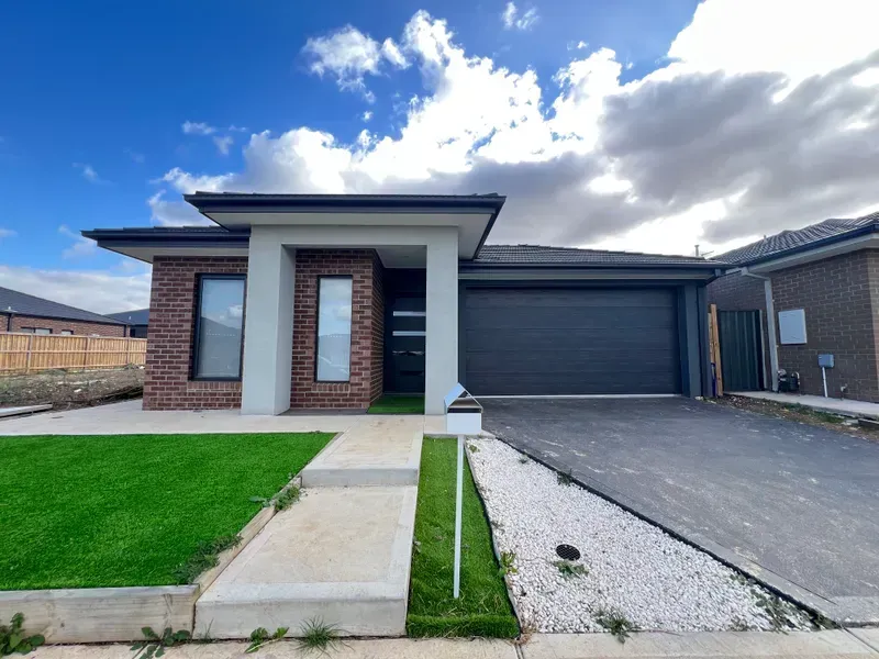 Modern home exterior with brick facade, black garage door, and green lawn under a cloudy sky.