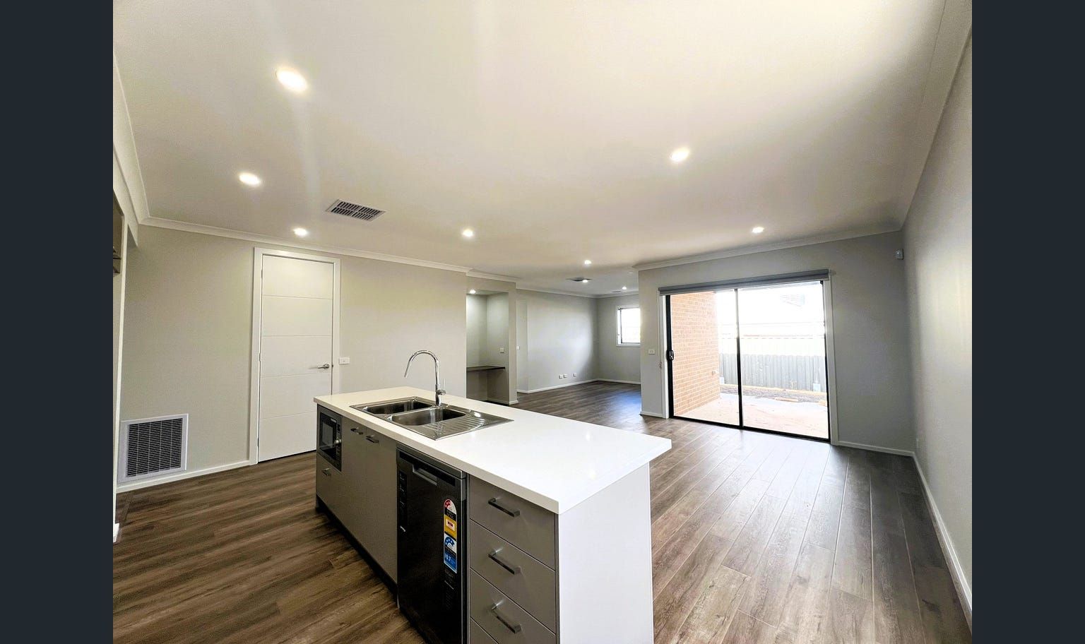 Interior of a modern kitchen and living area with a white island, gray cabinets, and large sliding doors.
