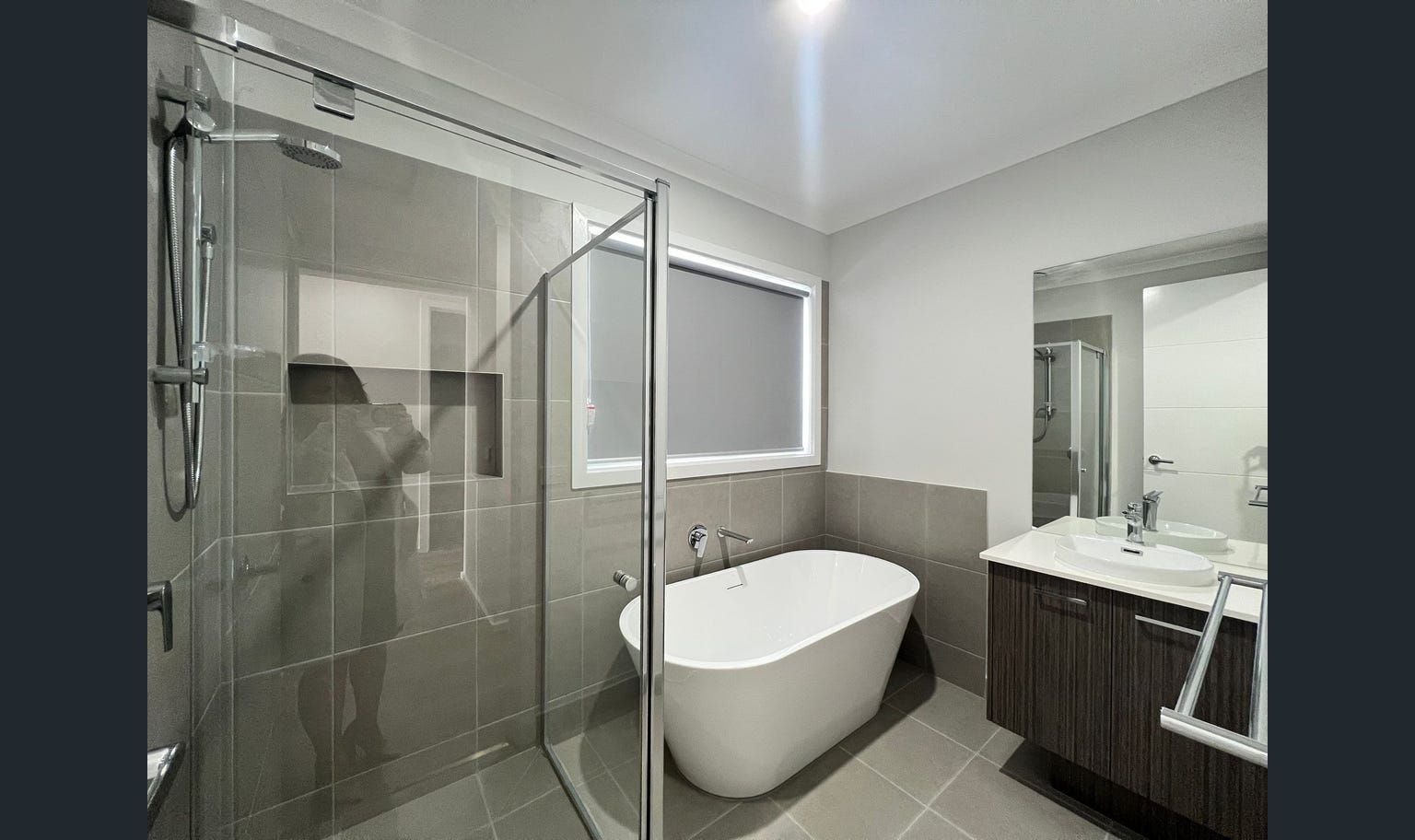 Modern bathroom with gray tile, a freestanding white tub, a shower, and a vanity with a dark wood cabinet.