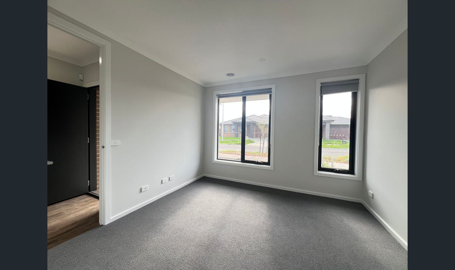 Empty bedroom with gray walls, carpet, and windows. Black door to the left.