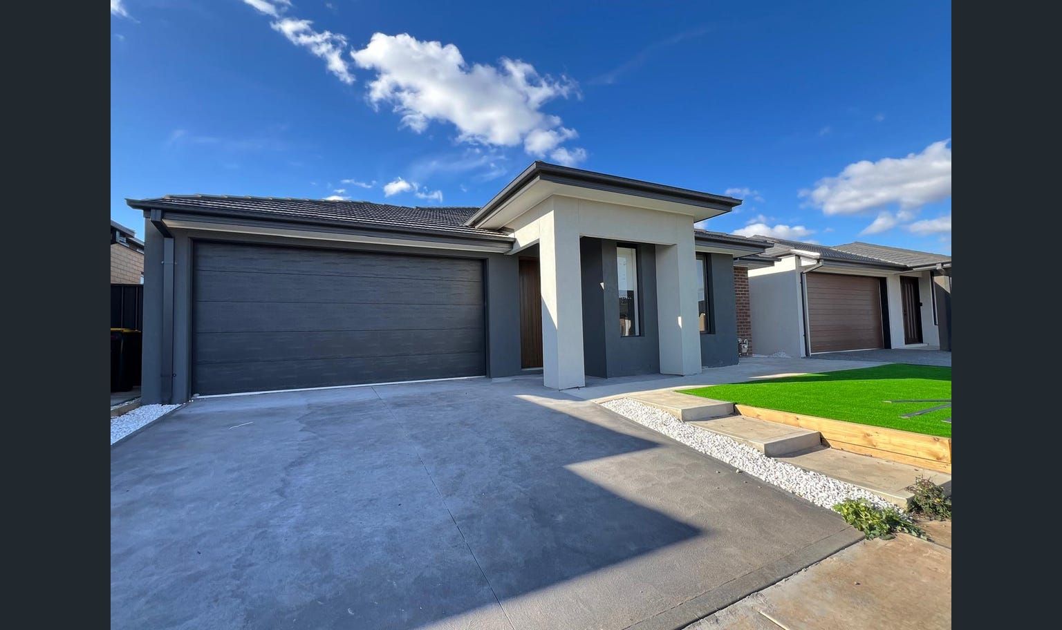 Modern suburban homes with gray garage doors and light-colored facades against a blue sky.