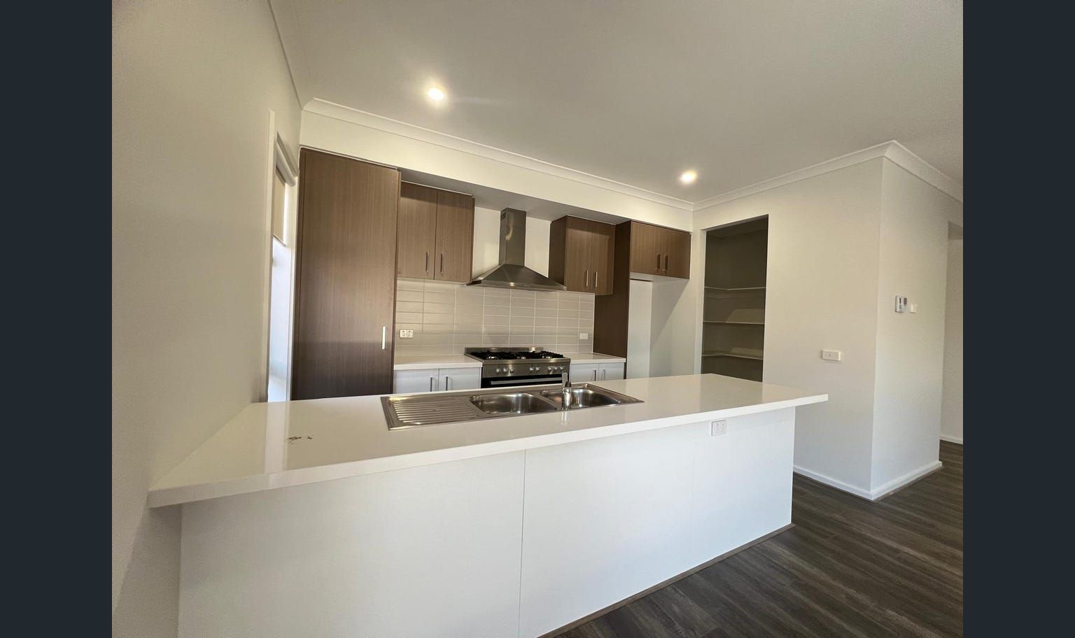 Modern kitchen with white countertops, dark wood cabinets, and a stainless steel range hood.