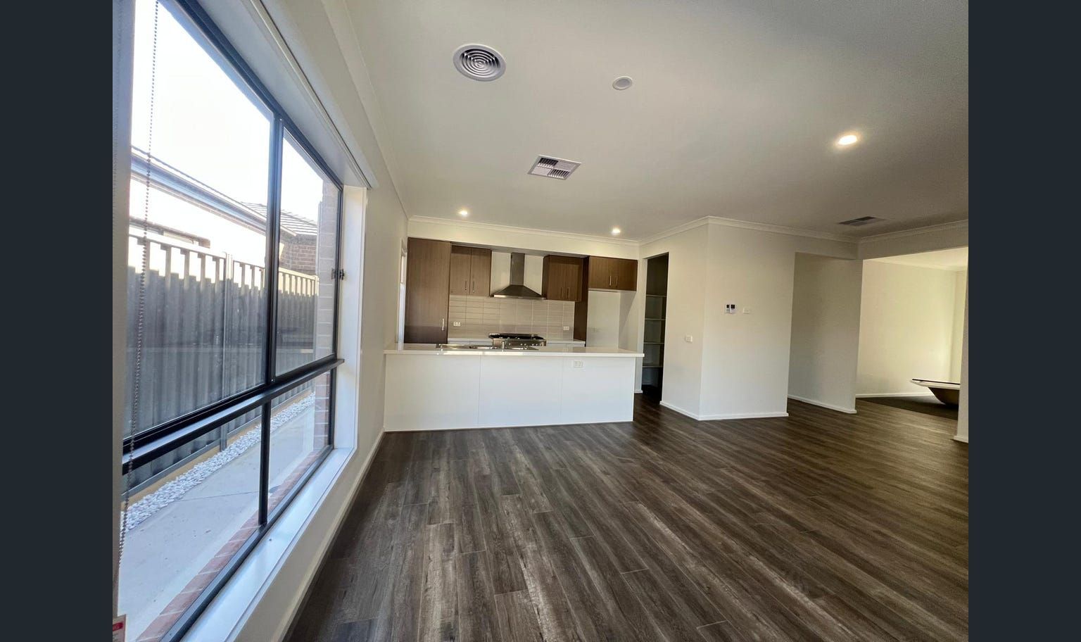 Interior view of a modern living space, open to a kitchen.  Dark wood-look flooring.