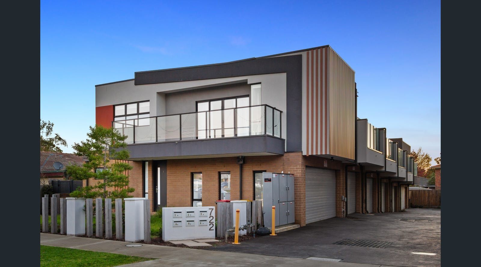 Modern multi-unit residential building with gray, orange, and brown facades. Features balconies.