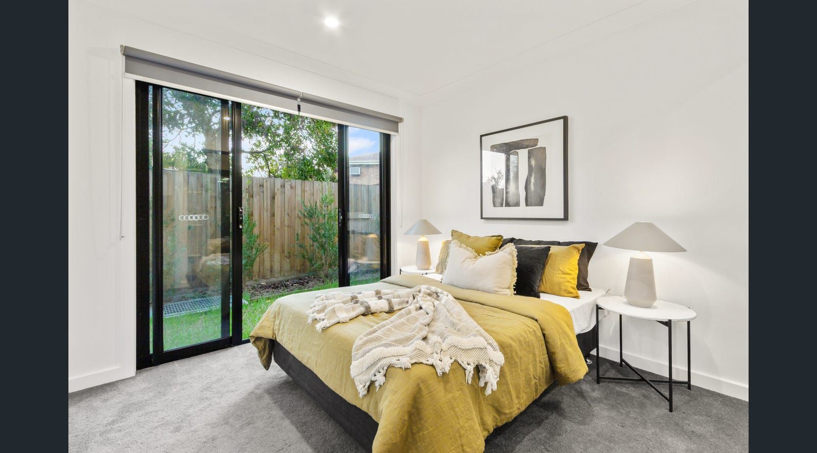 Bedroom with yellow bedding, artwork, and a sliding glass door leading to a small backyard.