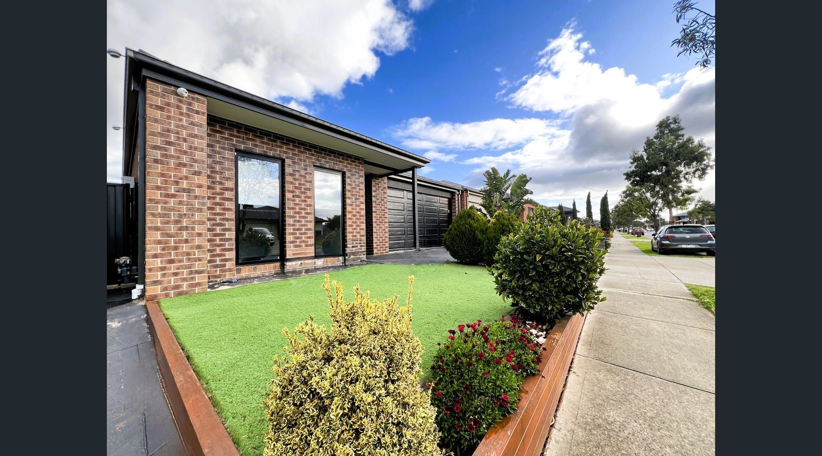 Modern brick house with black window frames, green lawn, and a sidewalk.