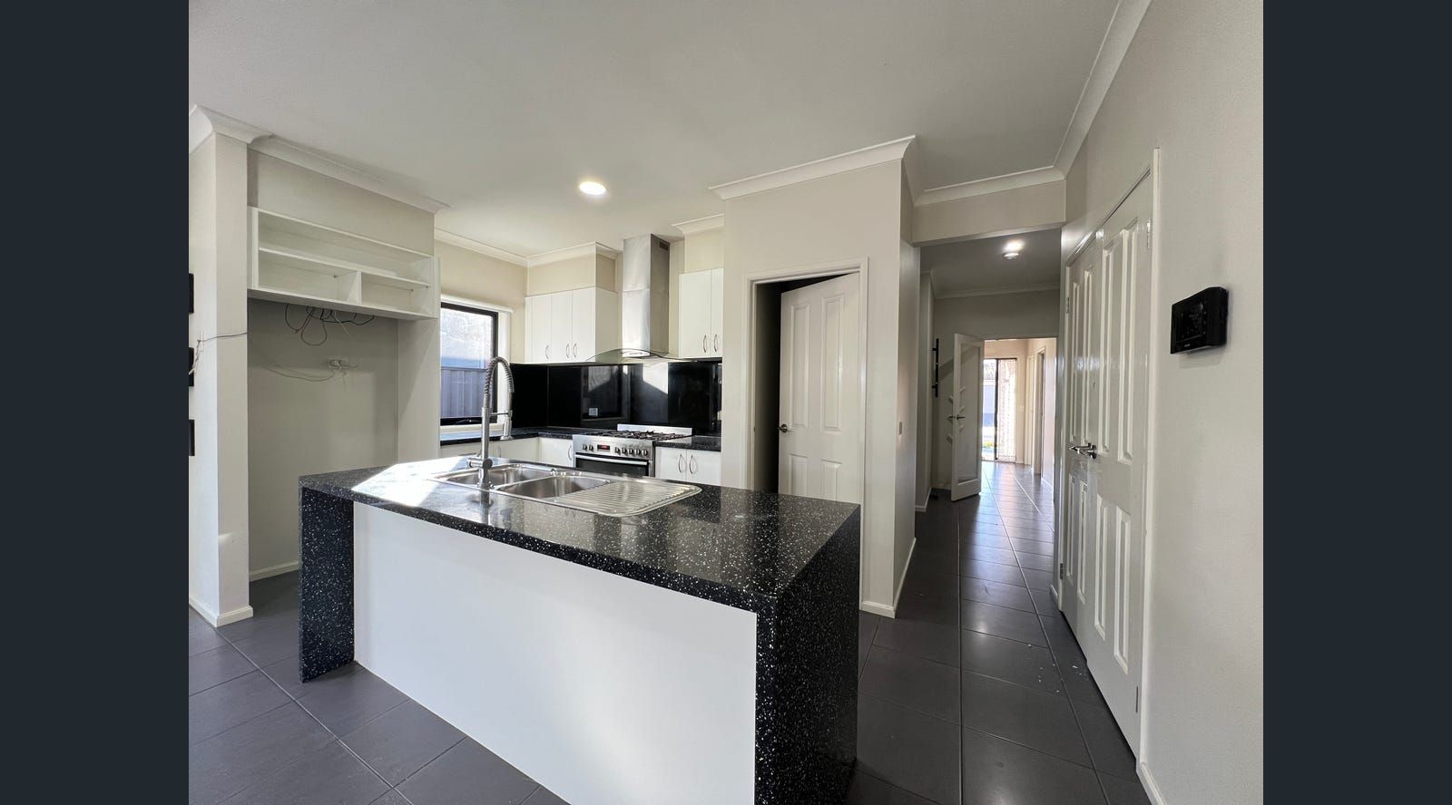 Modern kitchen with island, granite countertop, and stainless steel appliances. Hallway visible to the right.