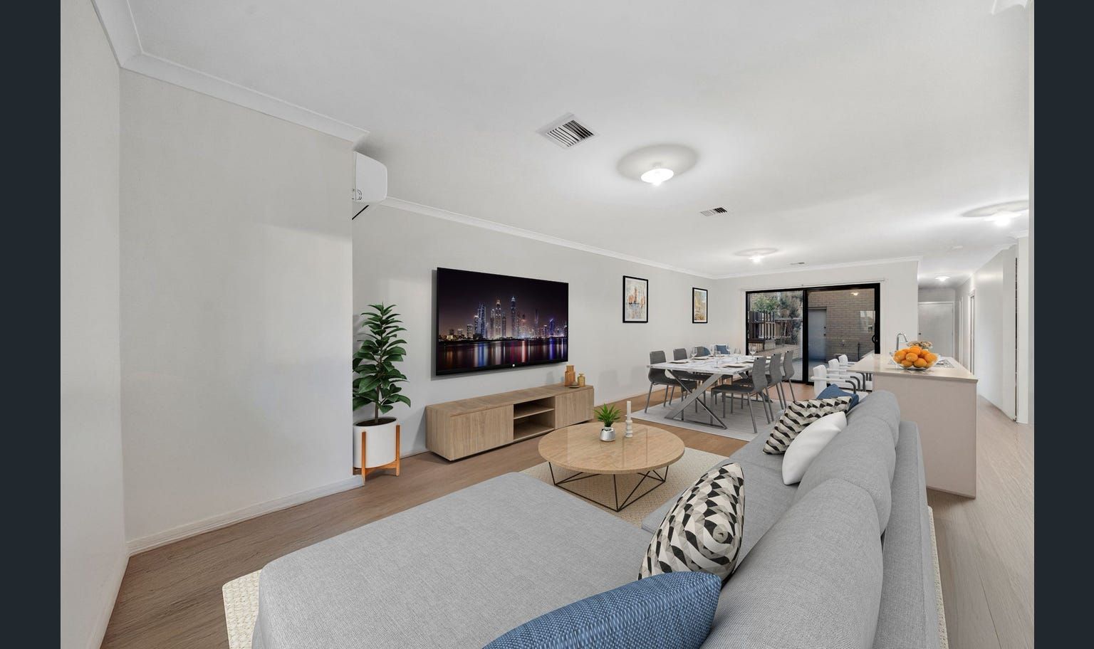 Spacious modern living room with gray sofa, TV, dining area, and a kitchen island.