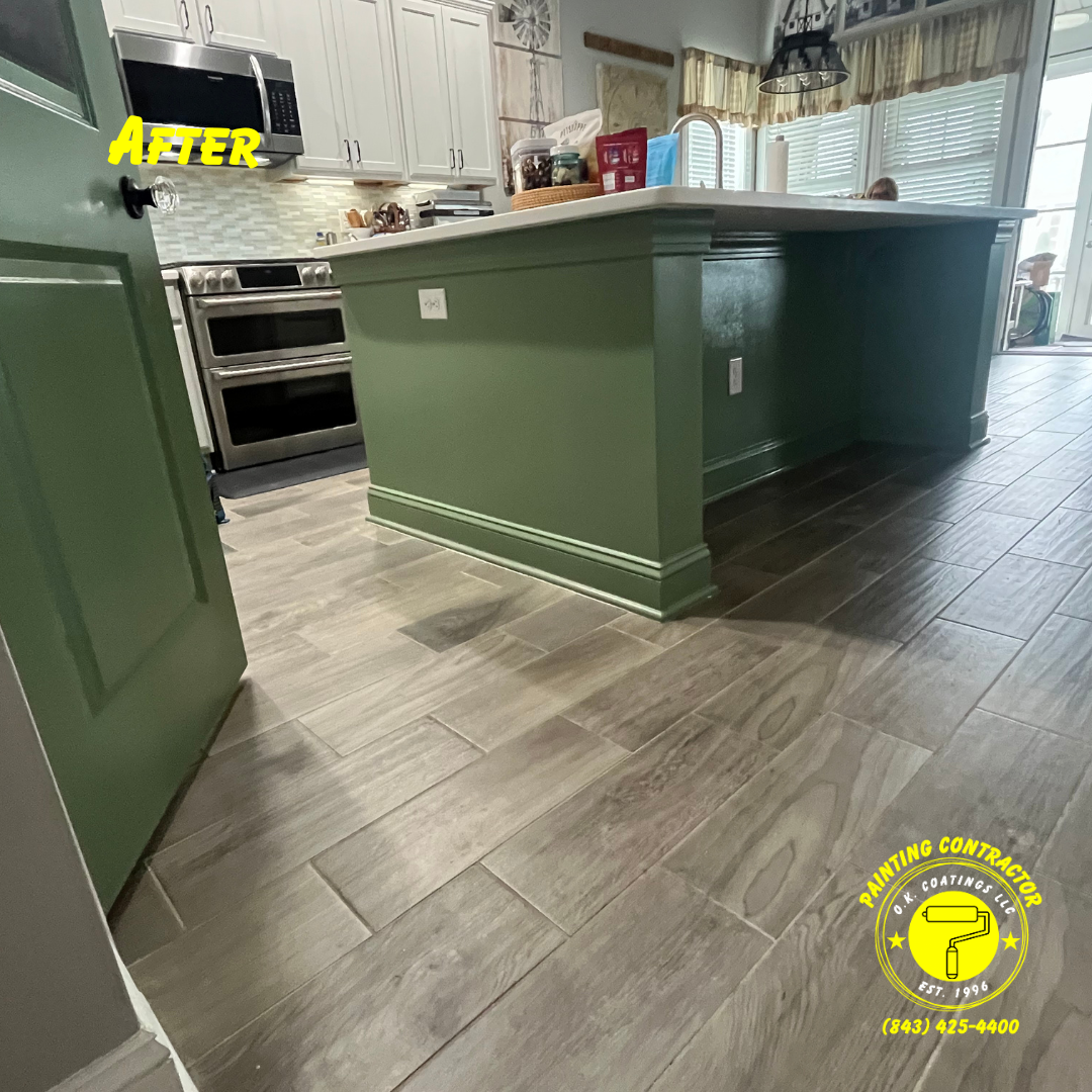 A kitchen island painted a muted olive green, set against light wood-look floor tiles, with a stainless steel range nearby.