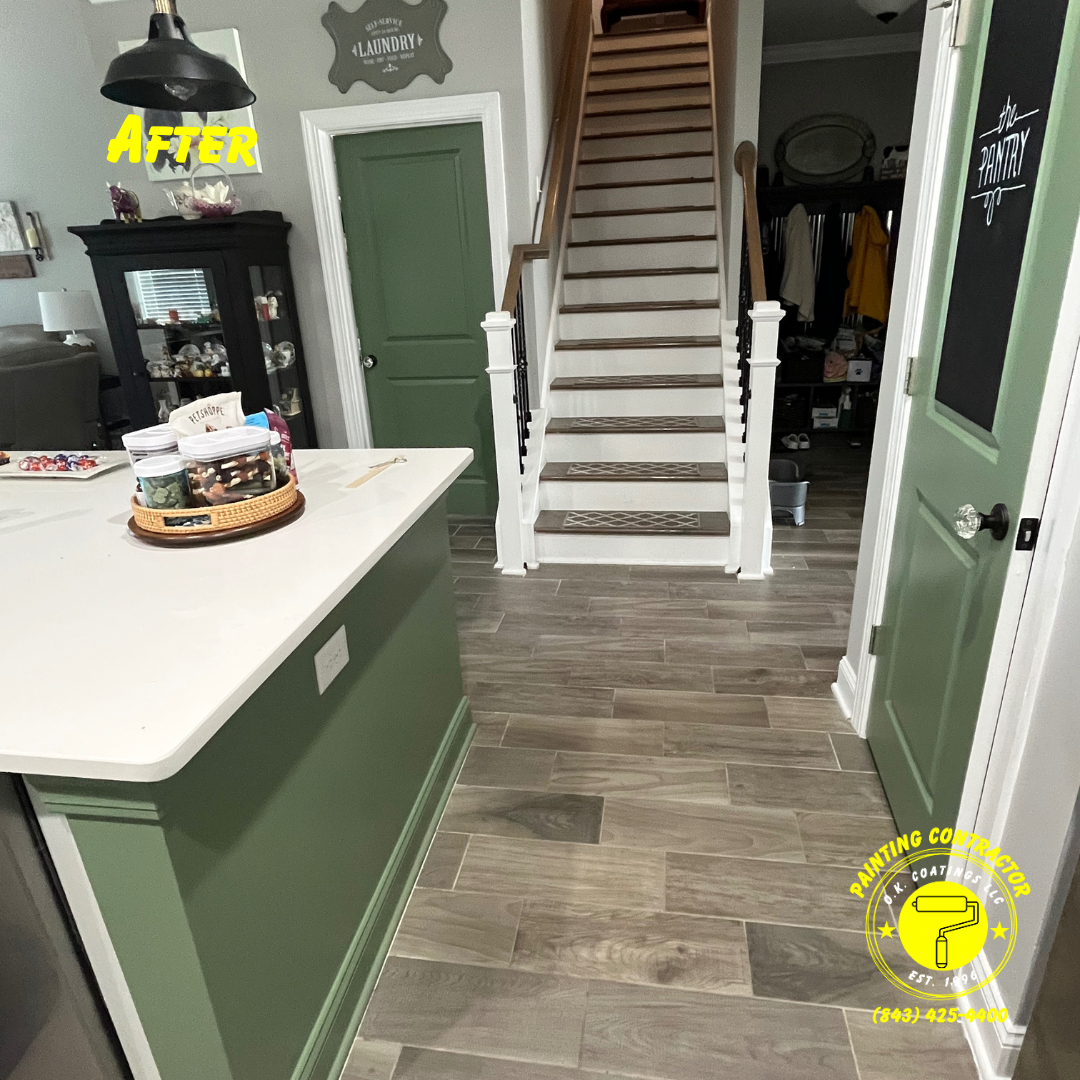 A kitchen island and doors painted sage green, next to a wooden staircase with white railings and gray wood-look flooring.