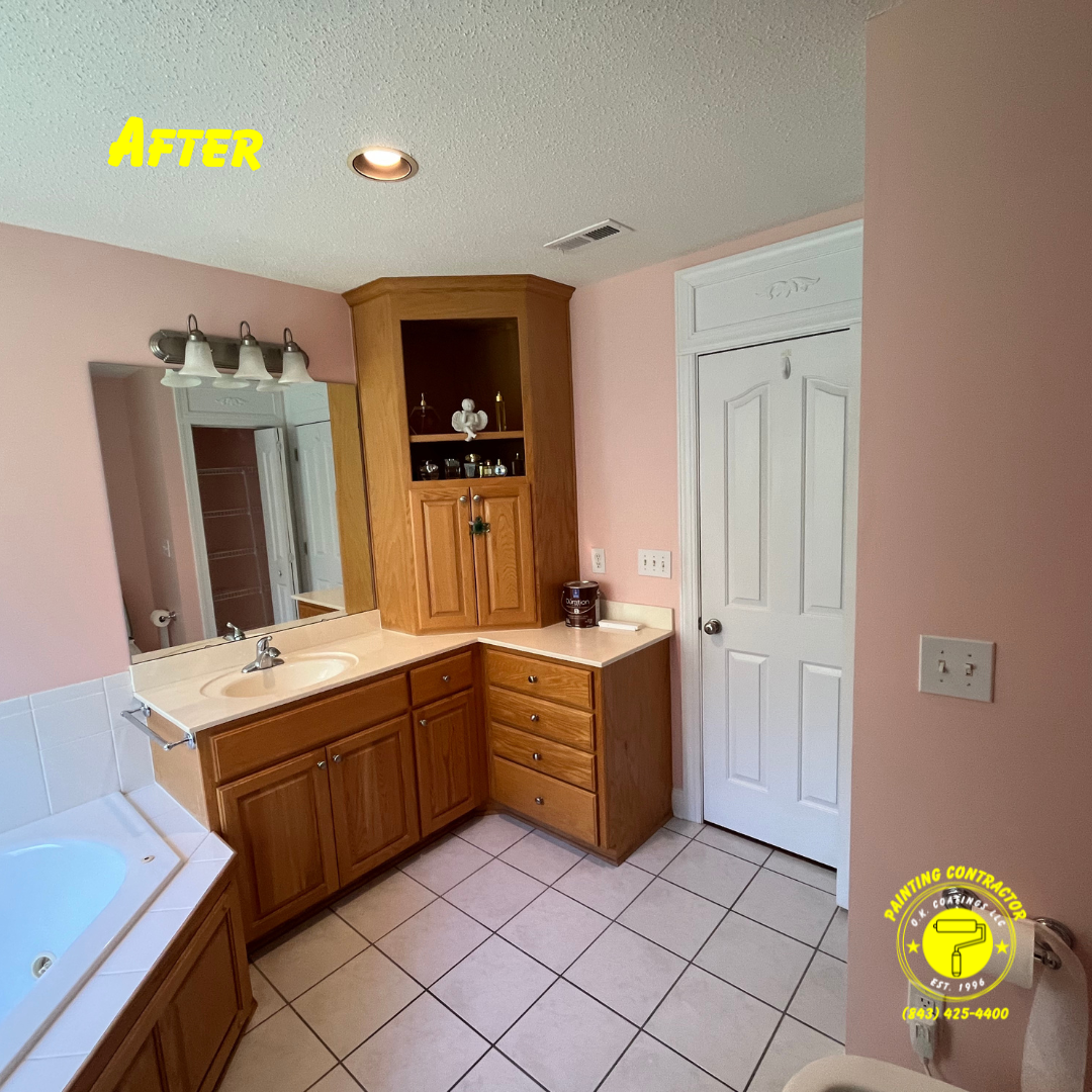 A bathroom with light pink walls, light wood cabinets, a corner storage unit, white doors, and tiled flooring.