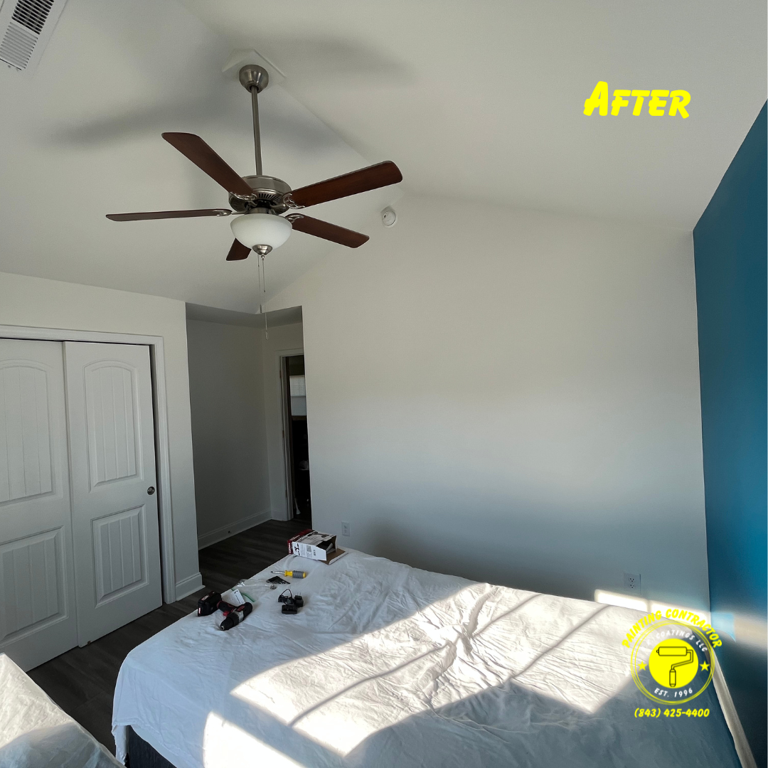 A bright bedroom features white walls, a blue accent wall, a white bed, and a ceiling fan. 