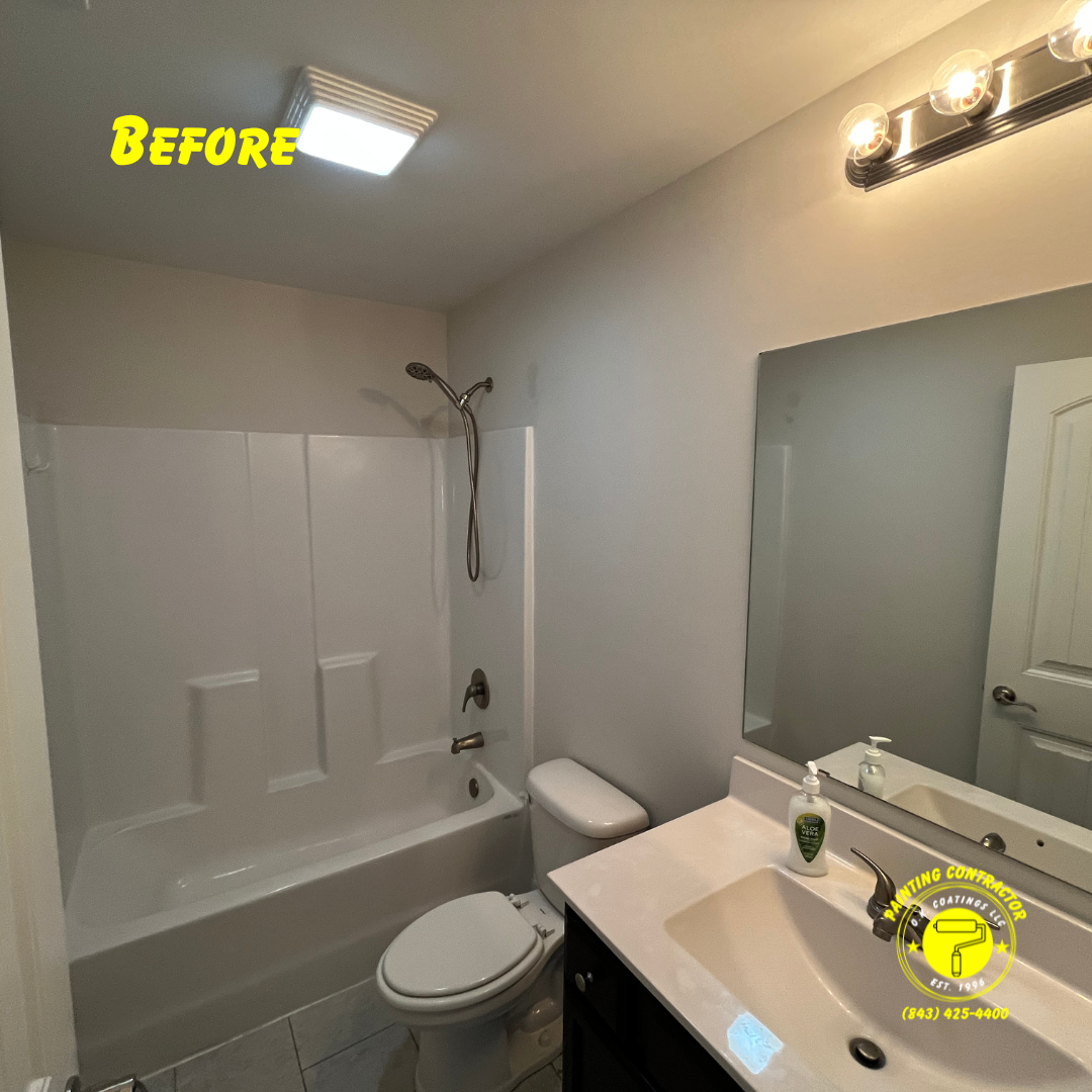 A bathroom with a white tub-shower unit, a toilet, a vanity with a white countertop, and a mirror before renovation.