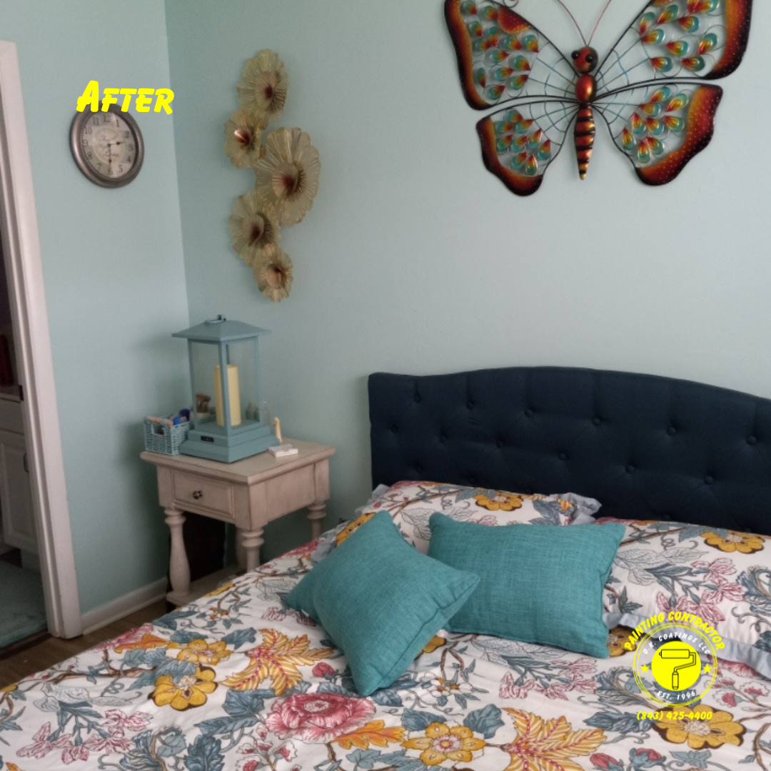 A decorated bedroom with a dark blue headboard, floral bedding, a teal lamp on a light wood nightstand, and wall decor.