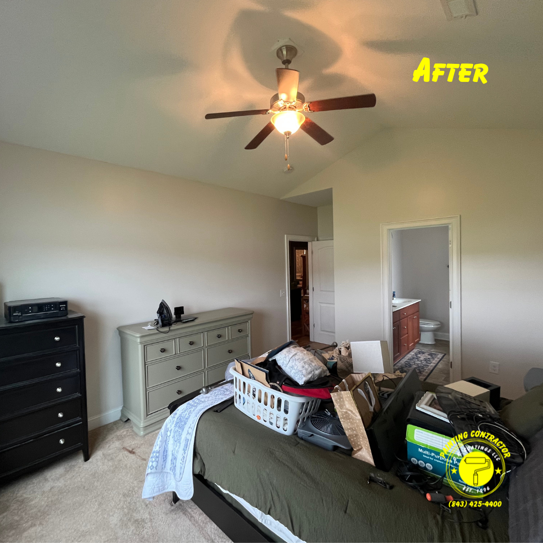 A bedroom with a ceiling fan, light beige walls, a black dresser, a large dresser, and a bed with items on top.