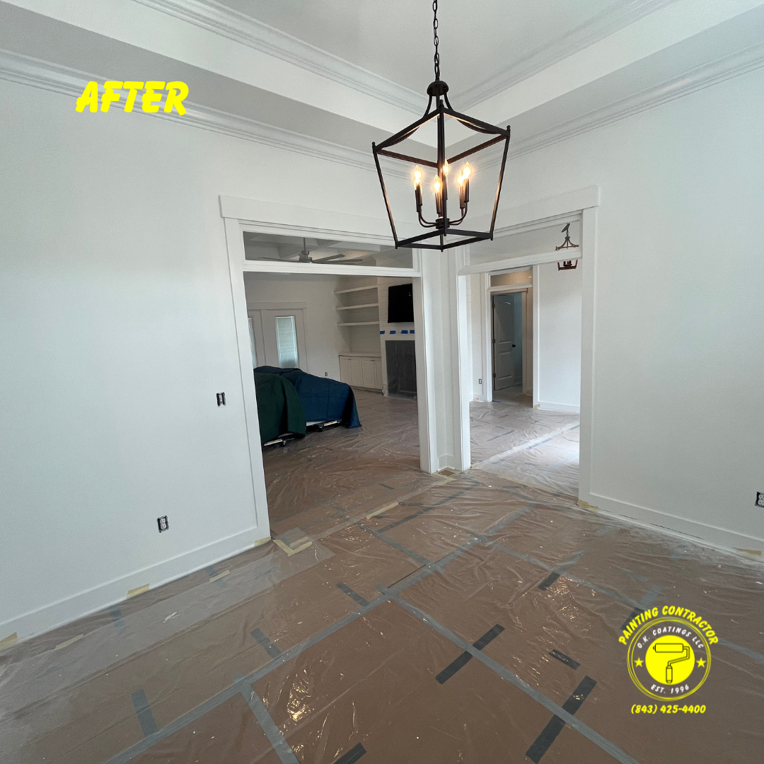 A dining room area painted white, featuring a black geometric lantern pendant light, with plastic covering the floor.