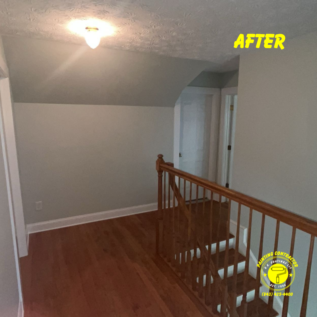 A view of a painted hallway with hardwood floors, a staircase with a wooden railing, and a central overhead light.