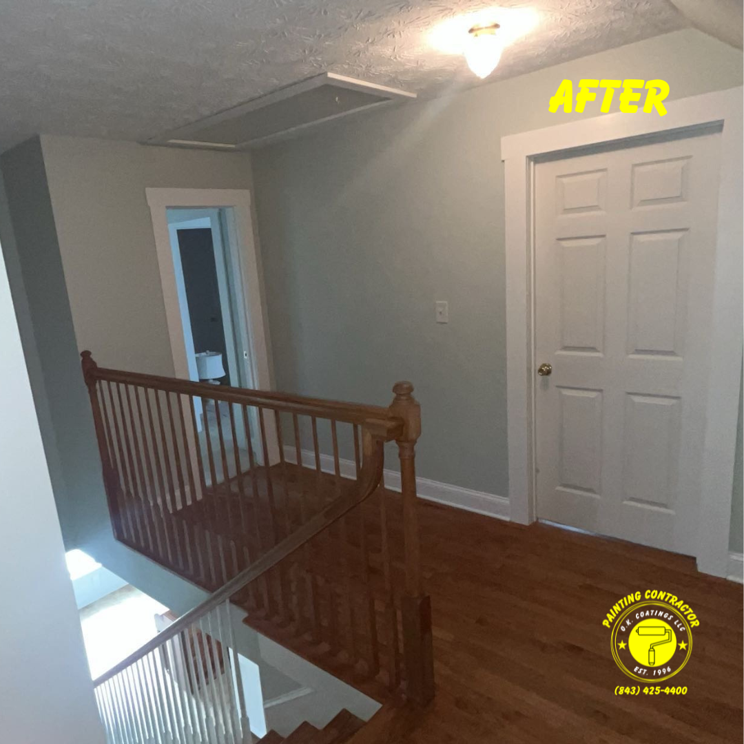 A hallway with light gray walls, wooden flooring, a wooden staircase railing, two white doors, and a ceiling light.
