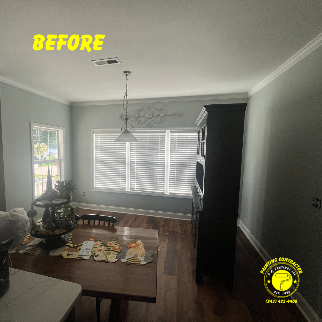 A before shot of a dining room featuring gray walls, wood floors, a dining table, a black hutch, and a window with blinds.