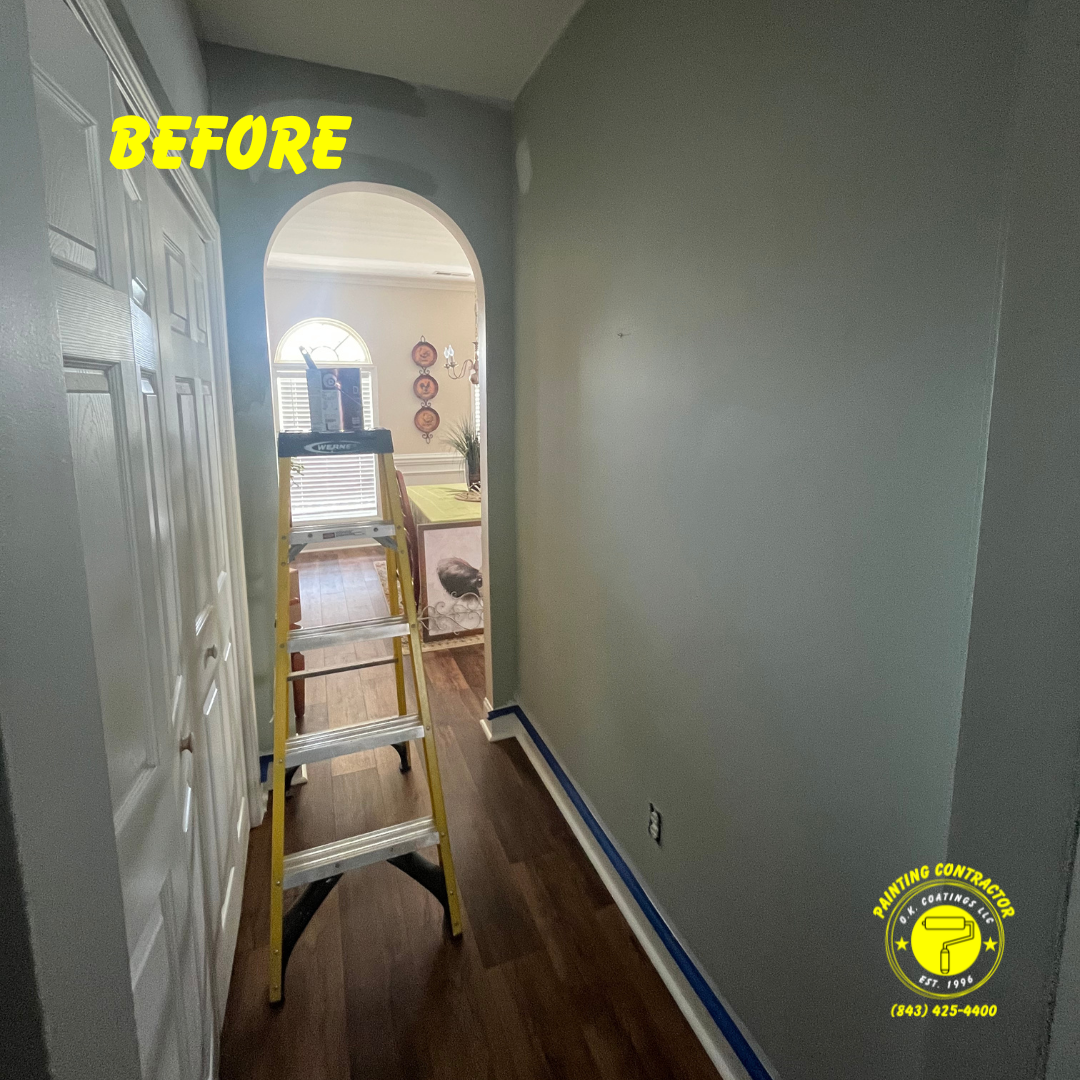 A hallway interior before renovation, showing grey walls, a yellow step ladder, and a dark wood floor.