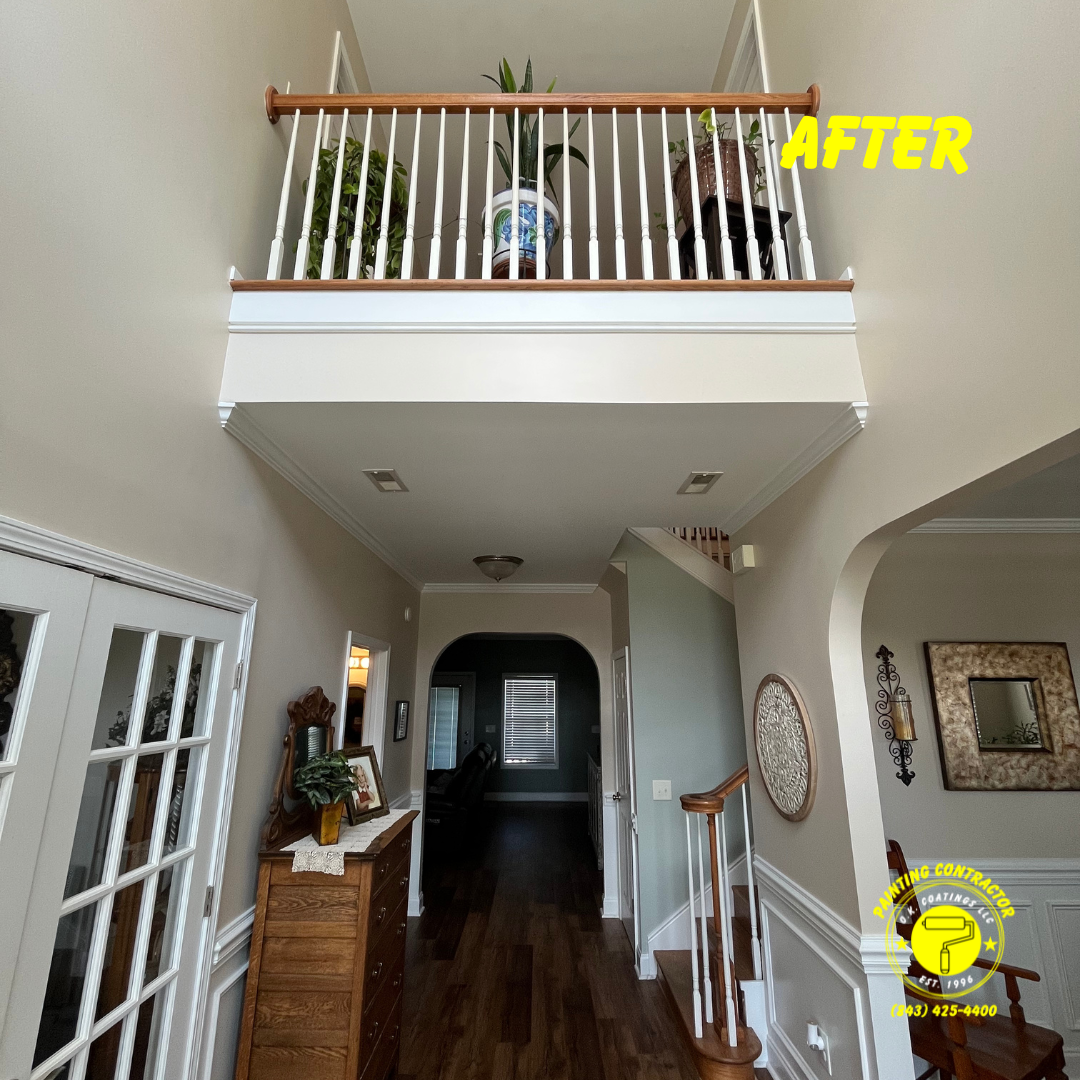 Interior view of a two-story entryway featuring a white wooden balcony railing, beige walls, and dark hardwood floors.