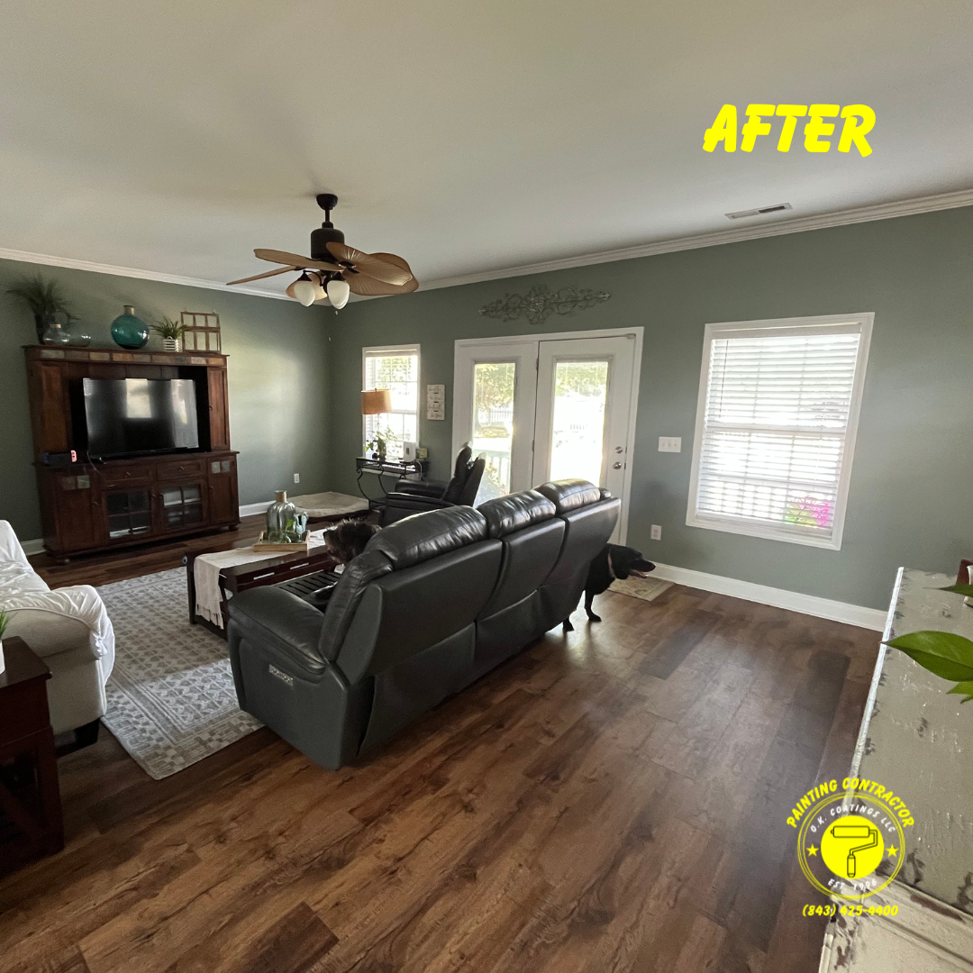A renovated living room with sage green walls, wood floors, a dark leather sofa, and a wood media console.