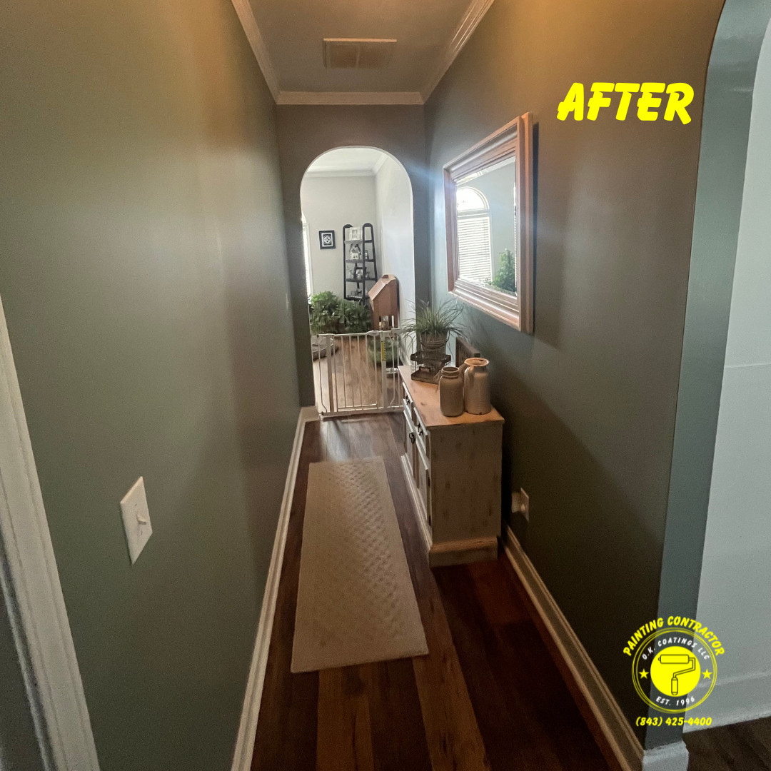 A narrow hallway with dark olive-green walls, hardwood floors, a beige runner, a side table, and a wall mirror.