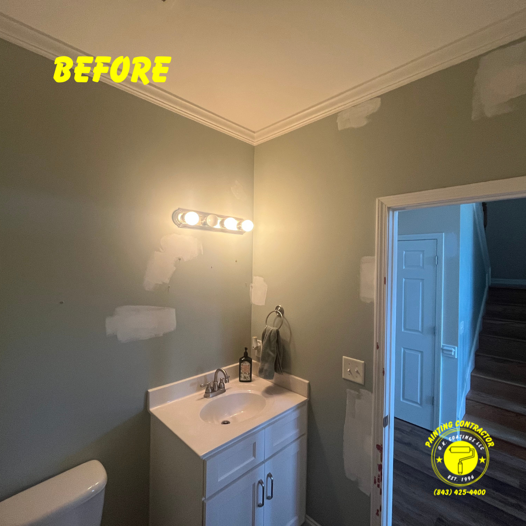 A sage green bathroom wall with multiple patches of white primer, an overhead vanity light, and a white sink.