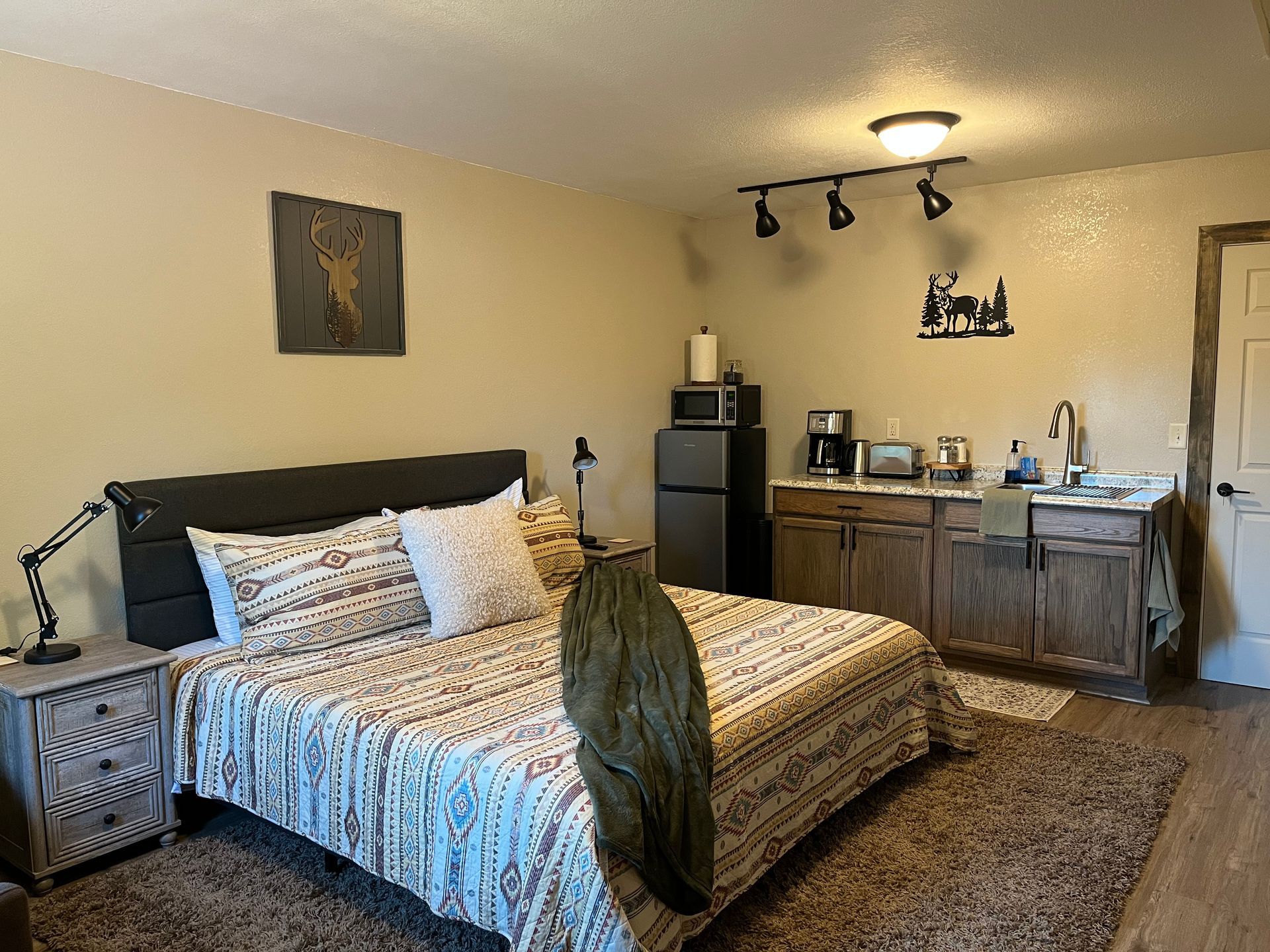 A bedroom with a bed , nightstand , refrigerator and sink.