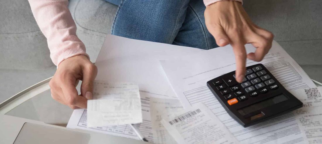 A Woman is Sitting on a Couch Using a Calculator — Rochdale Accounting & Business Advisory in Lismore, NSW