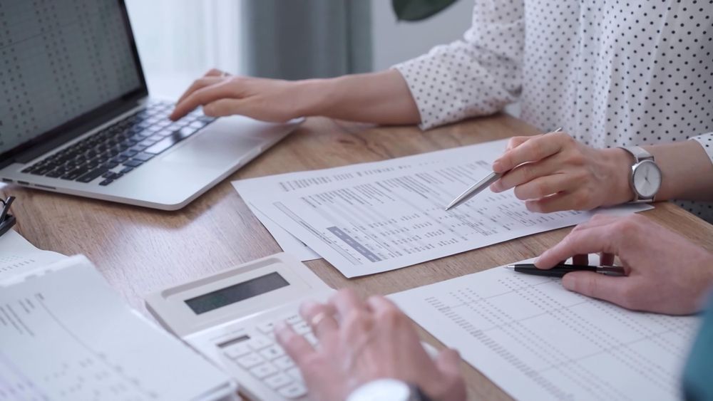 People at a desk, reviewing documents and using a laptop and calculator — Rochdale Accounting & Business Advisory in Alstonville, NSW