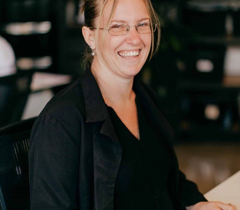 A Woman Wearing Glasses is Smiling While Sitting at a Desk — Rochdale Accounting & Business Advisory in Alstonville, NSW