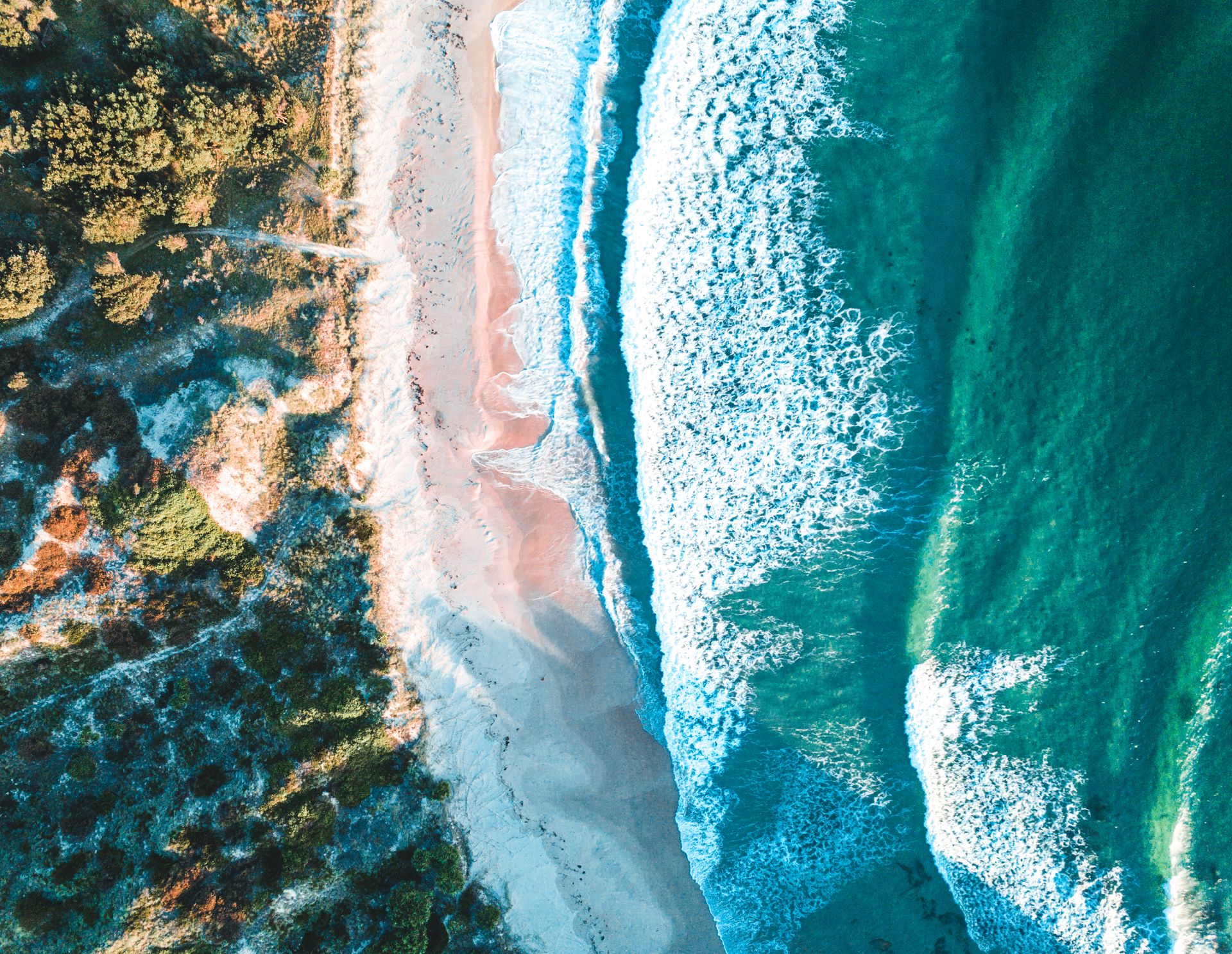 Aerial view of a sandy beach meeting the turquoise ocean with rolling white waves breaking along the shoreline — Rochdale Accounting & Business Advisory in Alstonville, NSW