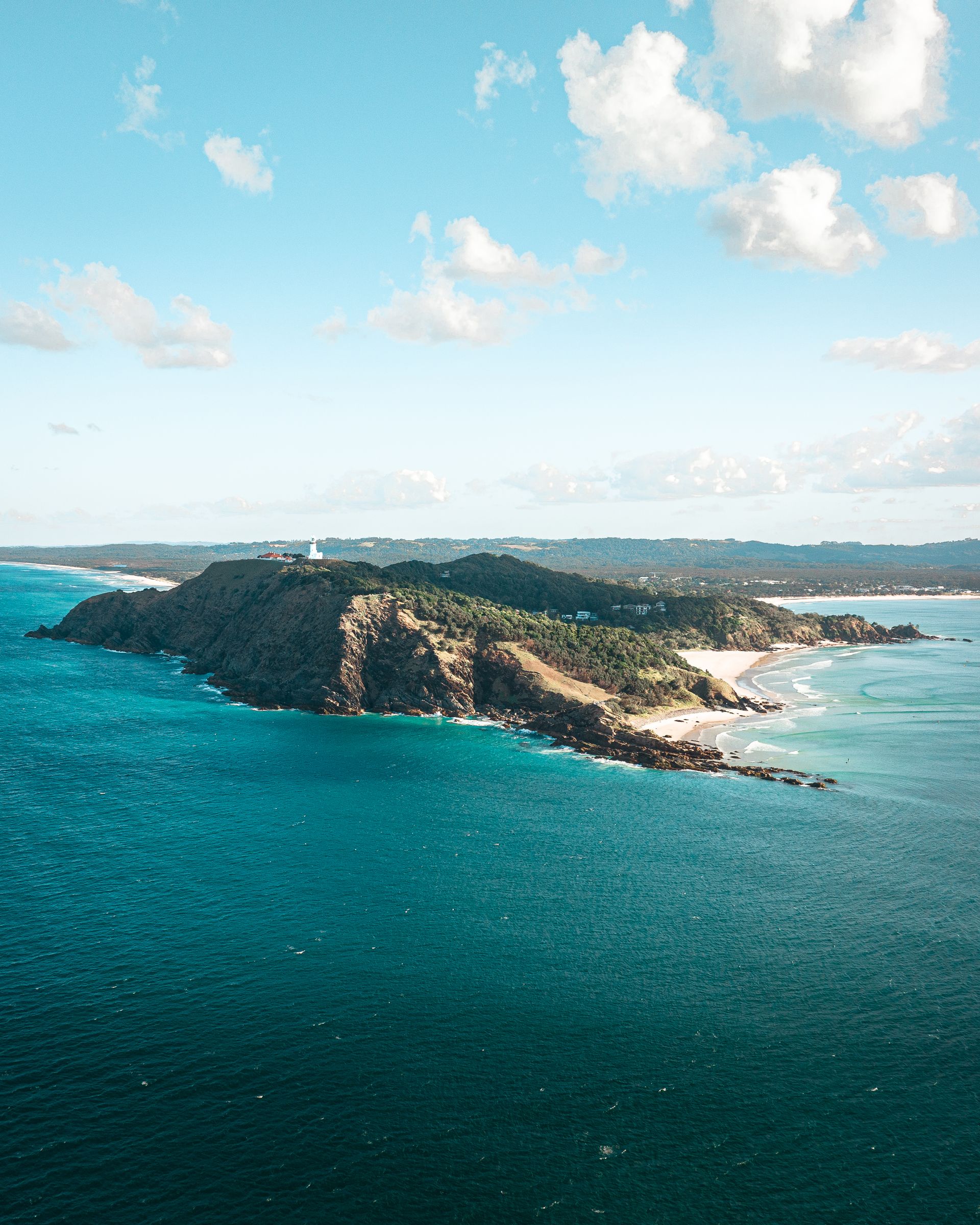 Aerial view of a turquoise coastline with a rocky cliff edge, green vegetation, and clear blue sky.
