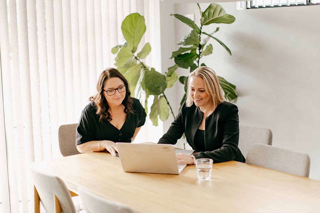 Two Women Are Sitting at a Table Looking at a Laptop Computer — Rochdale Accounting & Business Advisory in Bangalow, NSW
