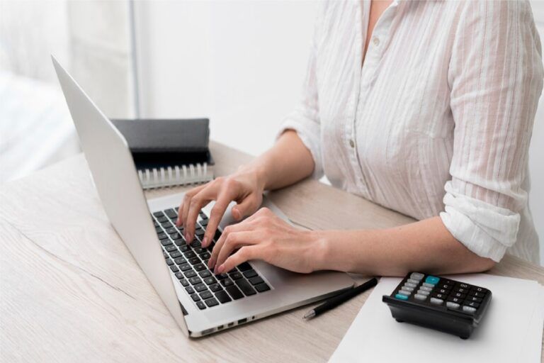 Person typing on a laptop at a desk with a calculator and pen — Rochdale Accounting & Business Advisory in Alstonville, NSW